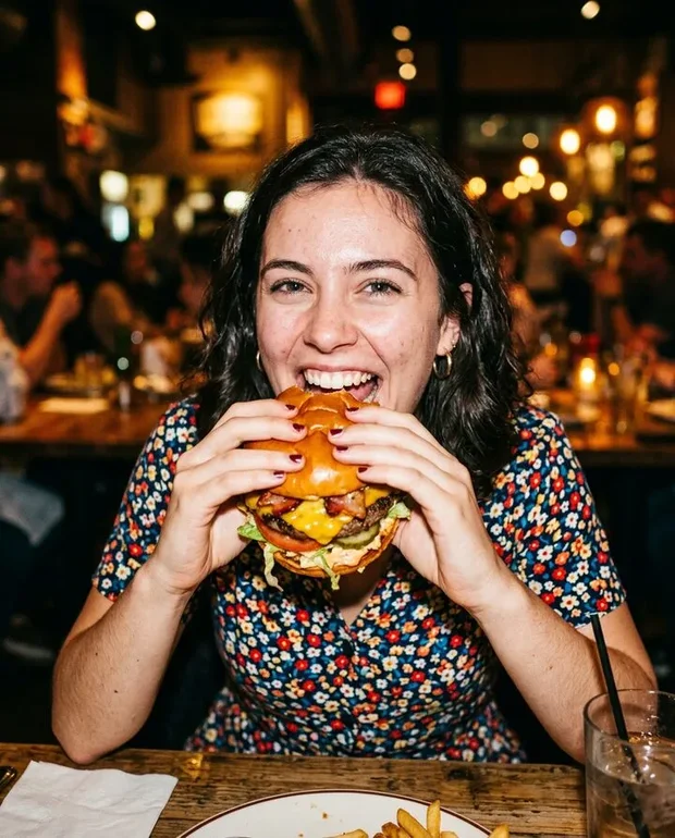 Vrouw neemt een grote hap van een volgeladen cheeseburger