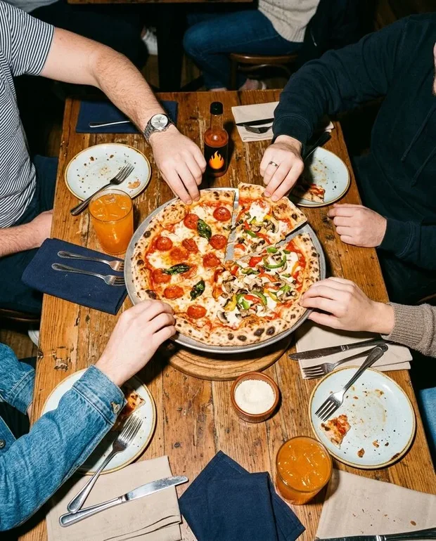 Tafel van bovenaf met pizza, glazen fris en handen die toetasten